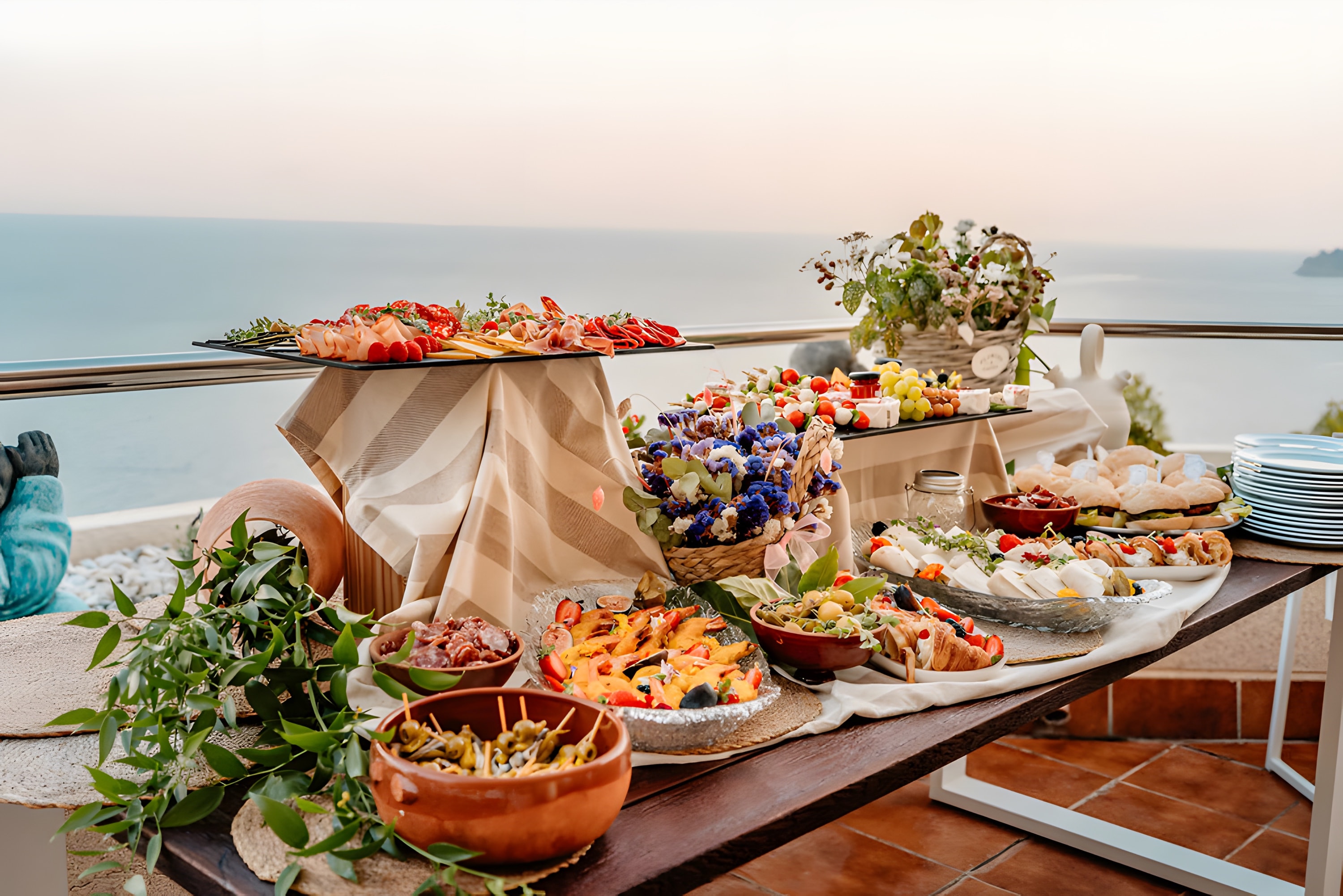 A dressed table on a terrace at golden hour, the sea glowing behind it