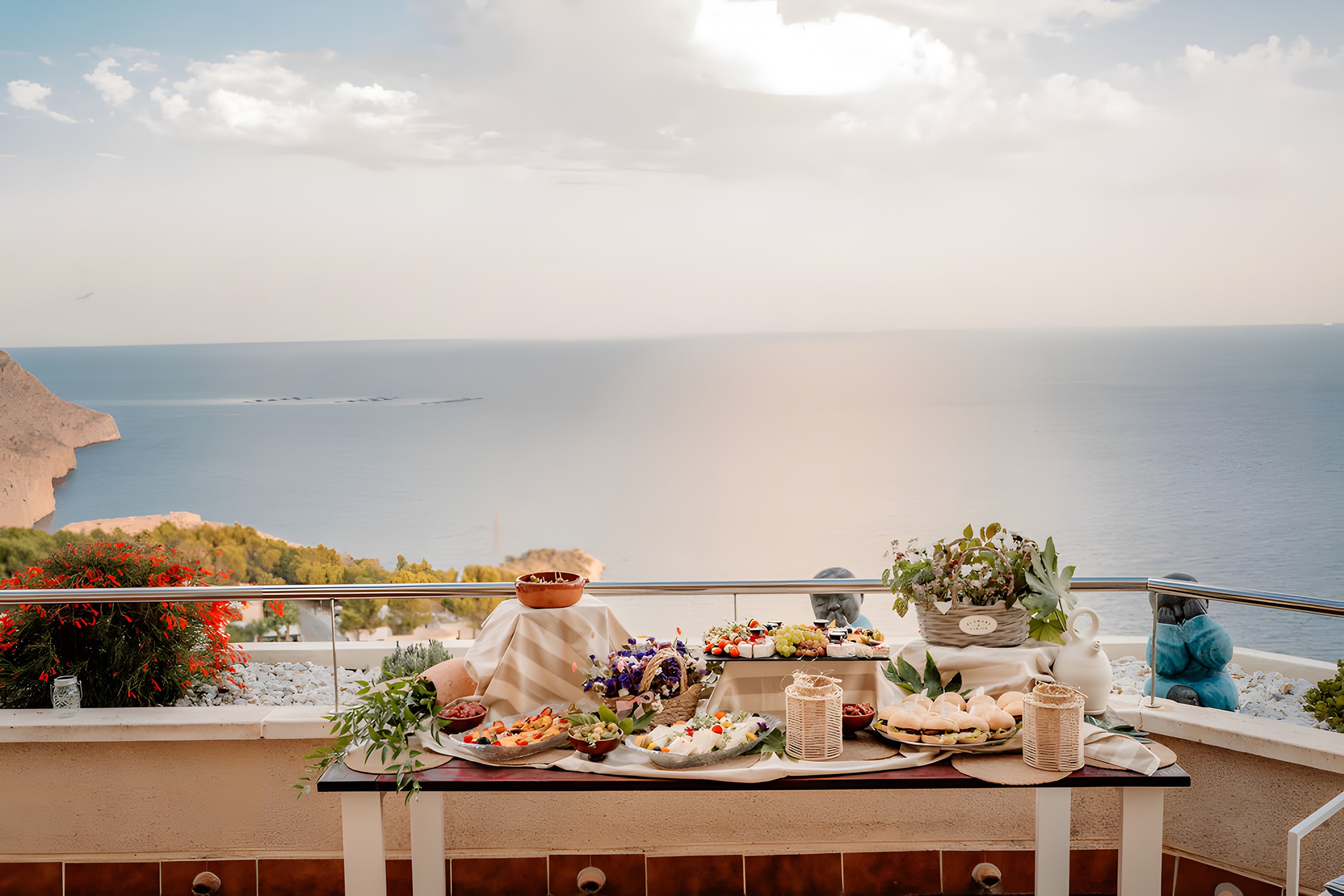 A quiet table setting on a terrace with a calm sea and soft sky beyond