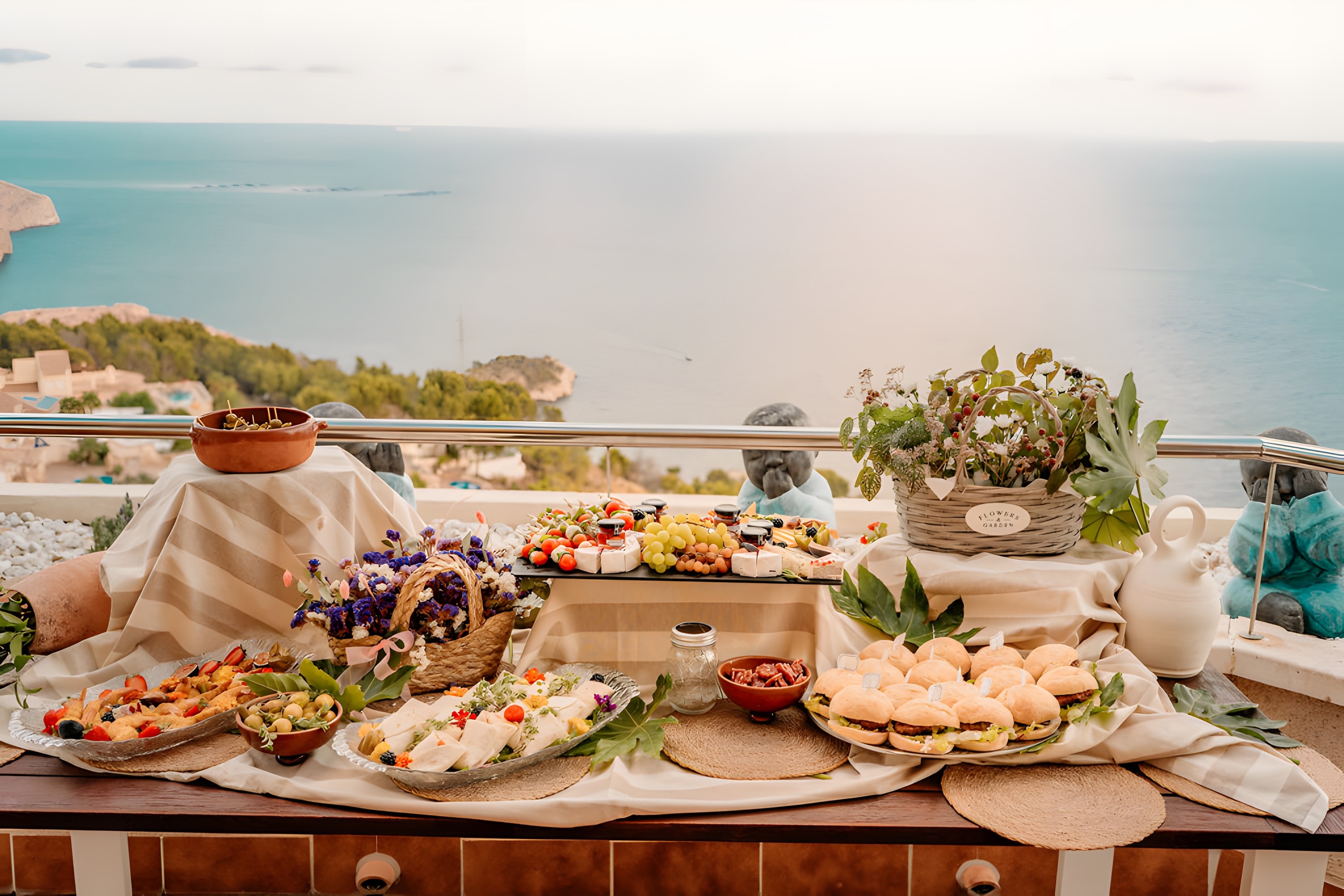 A long grazing table set on a villa terrace above the Mediterranean, with the Peñón de Ifach on the horizon