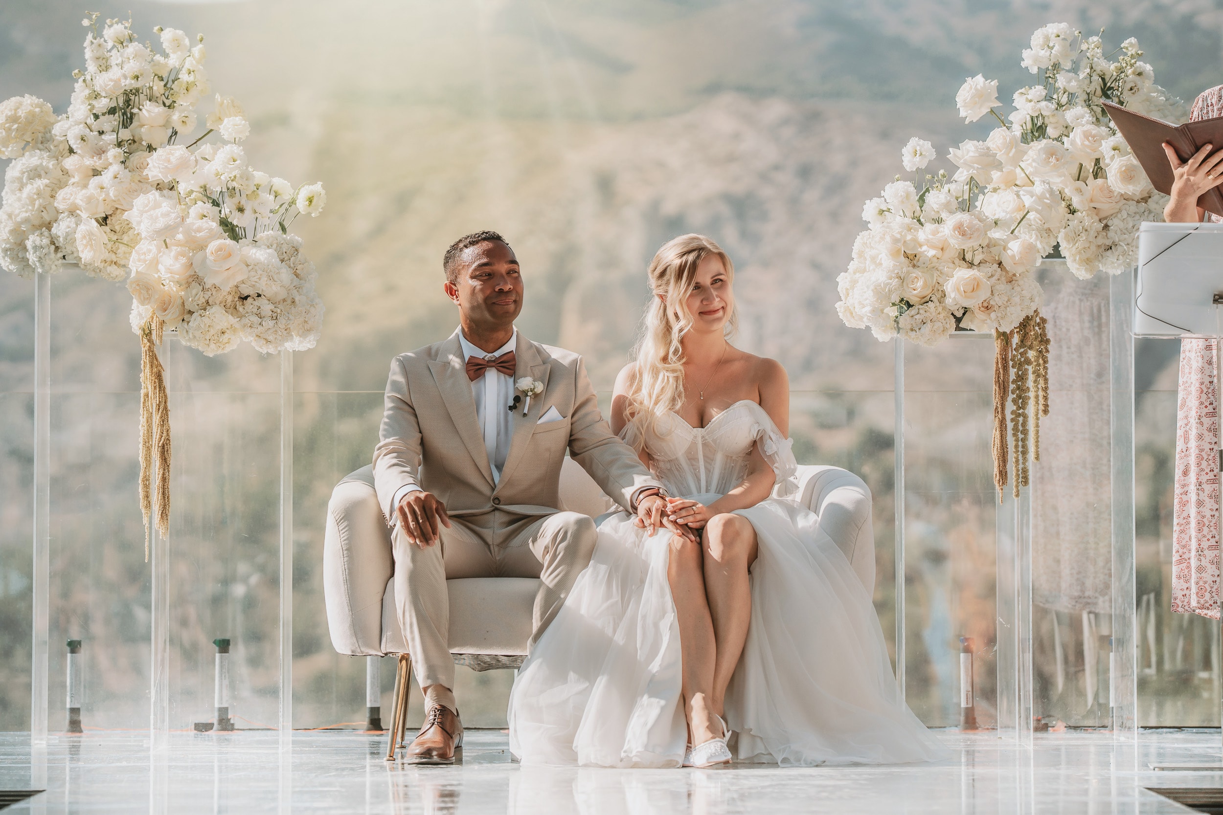 A couple seated at a white floral ceremony set against the mountains
